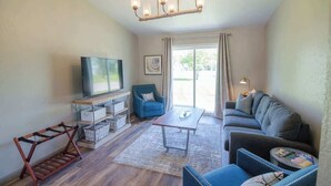 Ein Wohnzimmer mit einer Couch, einem Sessel, einem Fernseher und einem Holzregal.