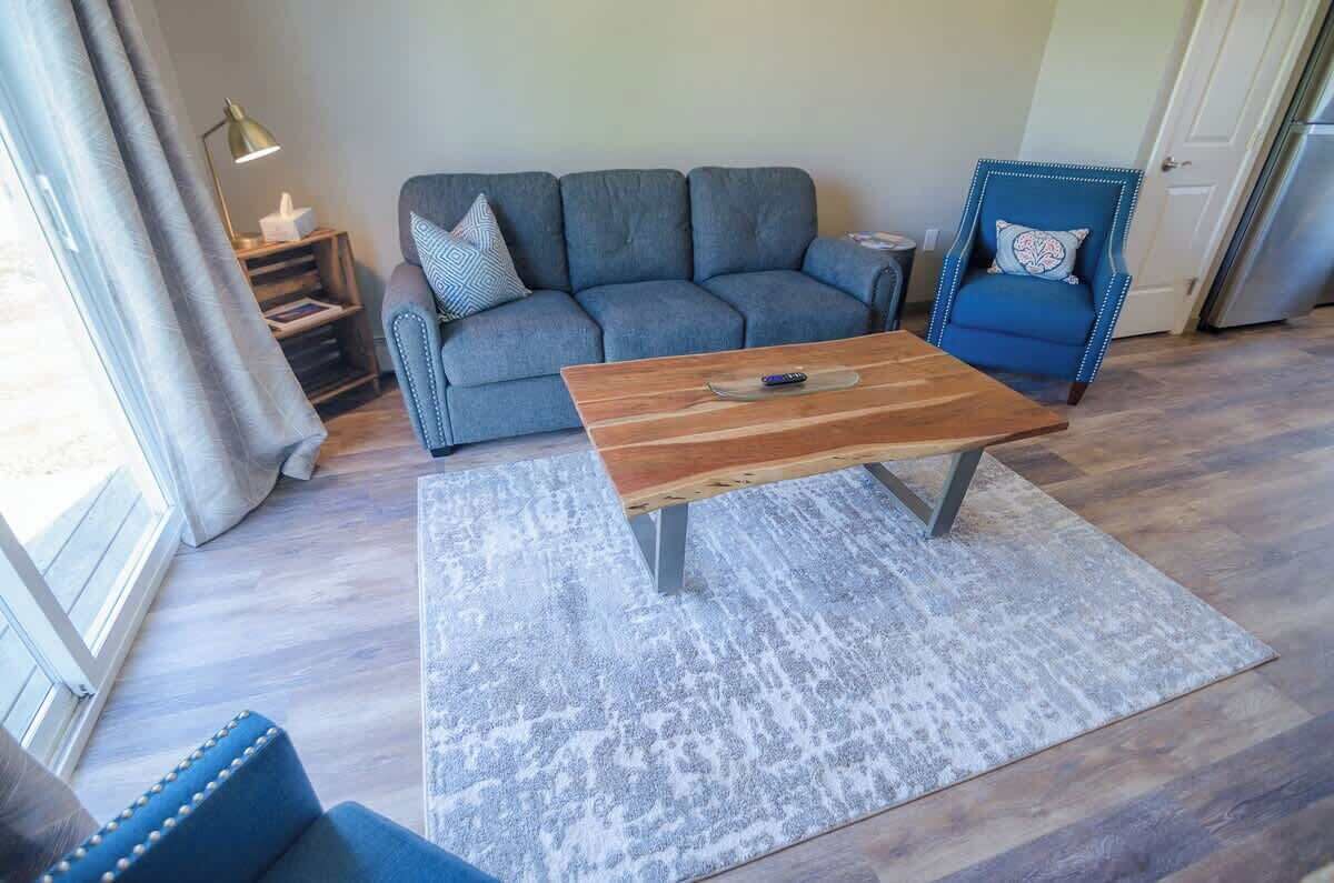 A living room with a grey sofa, a wooden coffee table, a blue armchair, and a patterned rug.