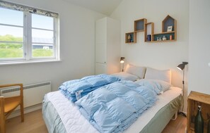 Een slaapkamer met een bed, een stoel, een bureau, een raam en wandplanken.