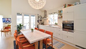 Et moderne køkken med hvide skabe, en indbygget ovn og et spiseområde med et træbord og orange stole.