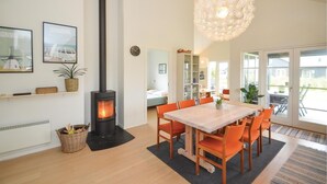 En moderne stue med en brændeovn, et spisebord med orange stole, og et stort vindue med udsigt til naturen.