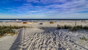 Een zandstrand met voetafdrukken die naar het water leiden, een houten hek en een heldere lucht.