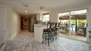A kitchen with a central island, bar stools, and a view of a patio with a thatched roof.