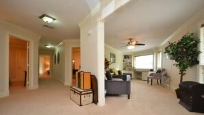 A spacious living room with a grey sofa, a coffee table, and a large window. There are suitcases stacked against the wall, indicating recent or upcoming travel.