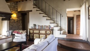 A spacious living room with a stone wall, a wooden staircase, and a bookshelf filled with books. - Spacious home on beautiful Tuscan vineyard.  Near Florence. (Pelago)