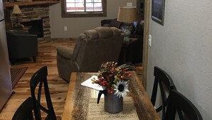 A dining area with a wooden table, chairs, a vase with flowers, a ceiling fan, and a stone fireplace. - #4 Fall Creek Cabins family friendly 1 mile from Lake Norfork , Mtn. Home Ar. (Mountain Home)