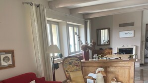 Una sala de estar con un sofá rojo, un sillón estampado, una mesa de centro de madera y una pequeña figurita de oveja blanca.