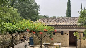 Un patio con muros de piedra, techo de tejas, mobiliario exterior y plantas en macetas.