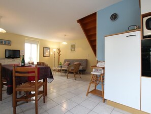 A dining area with a table and chairs, a sofa, a television, and a clock on the wall.