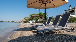 Un paisatge a la vora de la platja amb gandules i ombrel·les, una platja de pedres i un cel blau i clar.