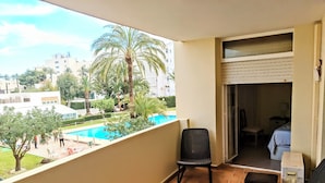 A balcony with two wicker chairs, a view of a swimming pool, and a building in the background.