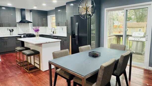 Une cuisine moderne avec des meubles de couleur sombre, un îlot central et un coin repas comprenant une table et des chaises.