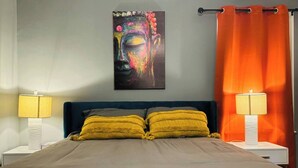 Une chambre à coucher avec un lit, deux lampes de chevet, un rideau orange et un tableau coloré accroché au mur.