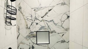 Un espace douche avec un mur en marbre, une pomme de douche noire et un porte-serviettes noir.