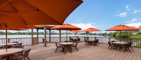 A deck with outdoor seating, orange umbrellas, and a view of a lake.