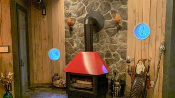 Una stanza rustica con una parete in pietra, rivestimenti in legno, un camino a legna rosso, una figura decorativa e un lampadario blu a forma circolare.