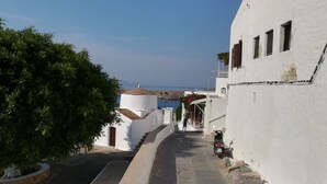 A narrow street with white buildings, a tree, and a scooter parked on the side.