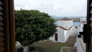 A view from a balcony with a tree, white buildings, and a distant coastline.