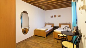 A small, well-lit room with a wooden ceiling, a bed, a desk with a chair, and a mirror.