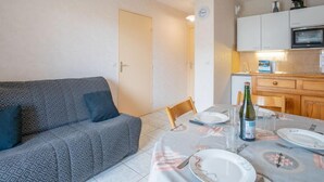 Un espacio habitable compacto con sofá, una mesa de comedor para dos personas y una kitchenette.