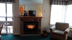 A living room with a fireplace, a television on a stand, a sofa, and a dining area with chairs. - 1BR condo near Recreation Center, pool and hot tub (North Woodstock)