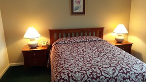 A bedroom with a bed, two bedside tables with lamps, a framed picture on the wall, and a wooden headboard. - 1BR condo near Recreation Center, pool and hot tub (North Woodstock)