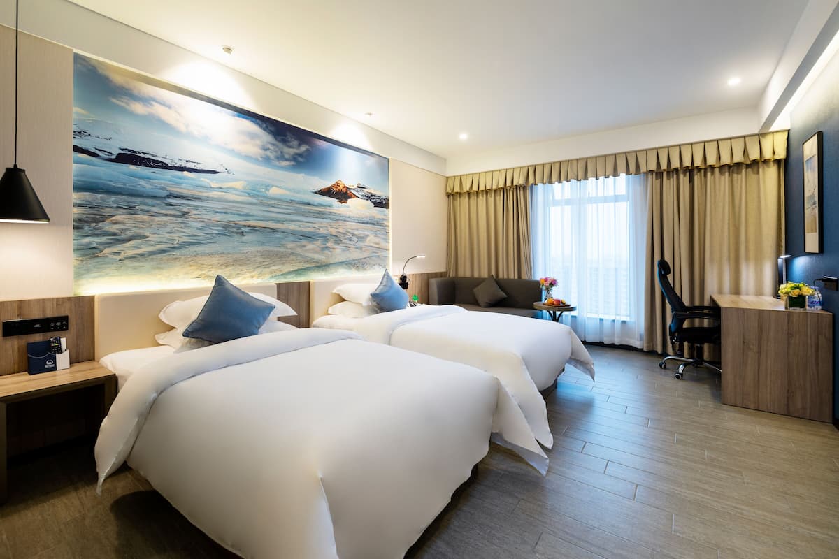 Habitación de hotel con dos camas, un escritorio, una silla y un cuadro grande de un paisaje marino.