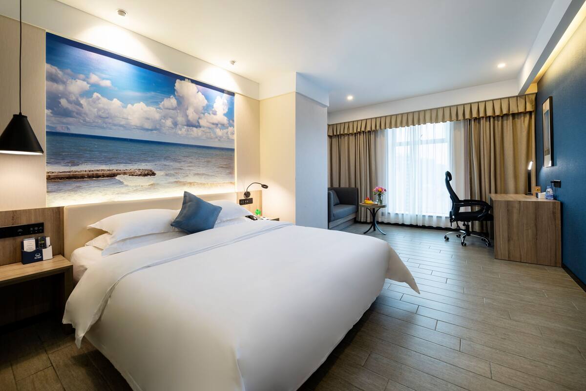 Habitación de hotel con una cama grande, un escritorio, una silla y vistas al océano a través de una ventana.