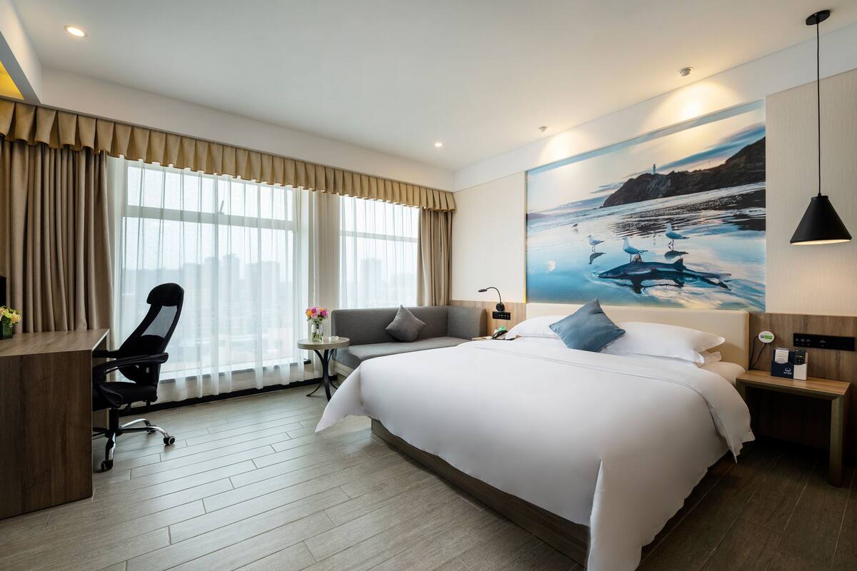 Habitación de hotel con una cama grande, un escritorio con silla, un sofá y un cuadro con gaviotas y una ballena en la pared.