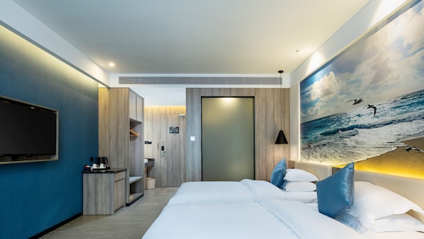 Una habitación de hotel moderna con una cama grande, un televisor de pantalla plana, un cuadro con surfistas en una ola y un armario de madera.