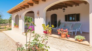 Un patio cubierto con mobiliario exterior, plantas en macetas y cielo despejado.