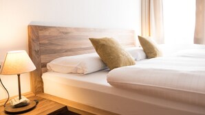 Ein ordentlich bezogenes Bett mit weißen Leinen und zwei Kissen, ein Holz-Kopfteil, eine Nachttischlampe und ein Nachttisch aus Holz.