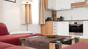 Ein modernes Wohnzimmer mit einem roten Sofa, einem Glastisch mit einer Schale, einer Lampe und einer Küche im Hintergrund.