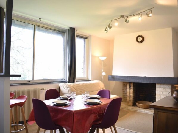 Un comedor con una mesa dispuesta para cuatro personas, una chimenea y un ventanal con cortinas.