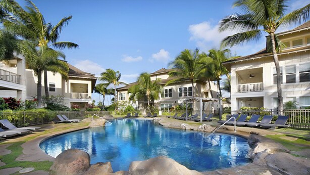 A pool area with lounge chairs, palm trees, and a two-story building with balconies. - 3BR/3BA Villa, Central A/C, Resort Style Complex, 5 Minute Walk To Poipu Beach! (Koloa)