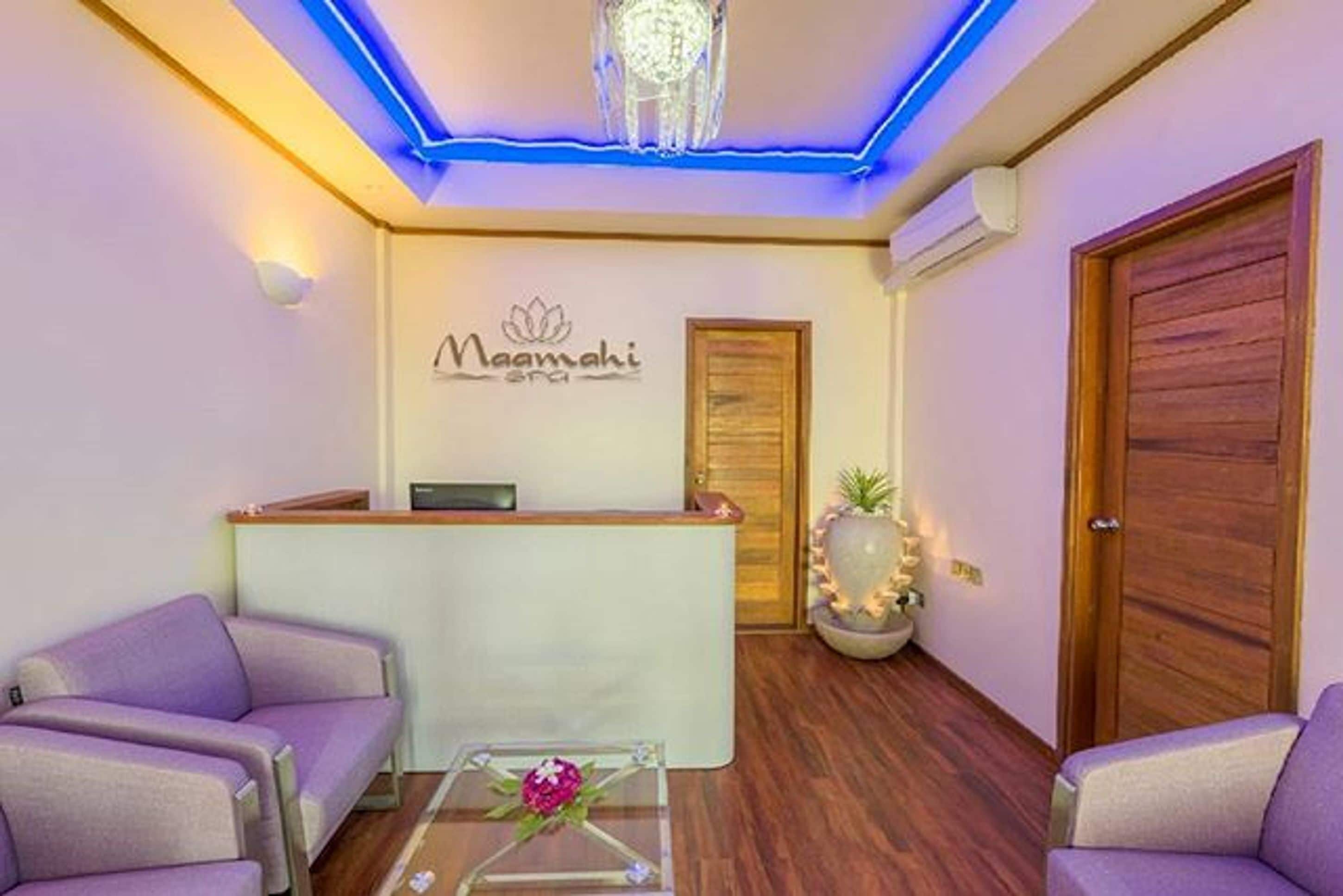 A reception area with a reception desk, two purple sofas, a small table with a vase, and a wooden door.