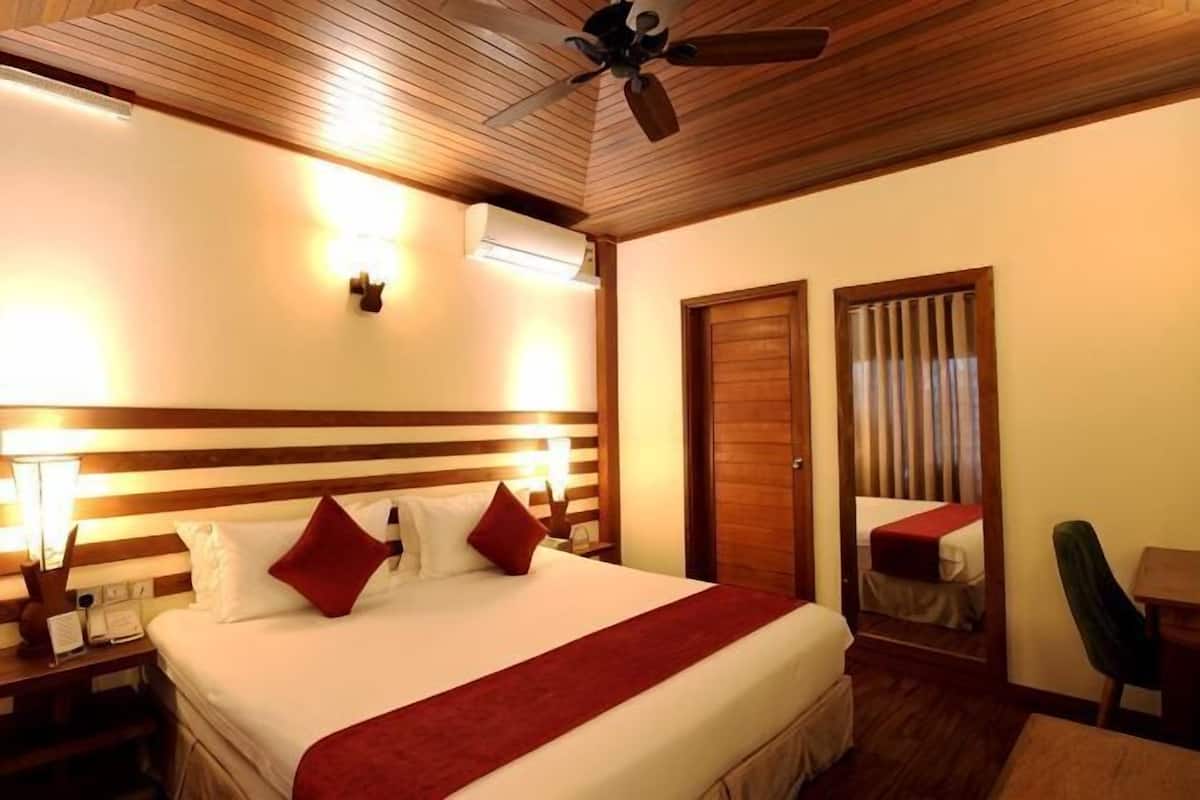 A hotel room with a bed, bedside lamps, a ceiling fan, a wooden headboard, a nightstand, a chair, and a door.