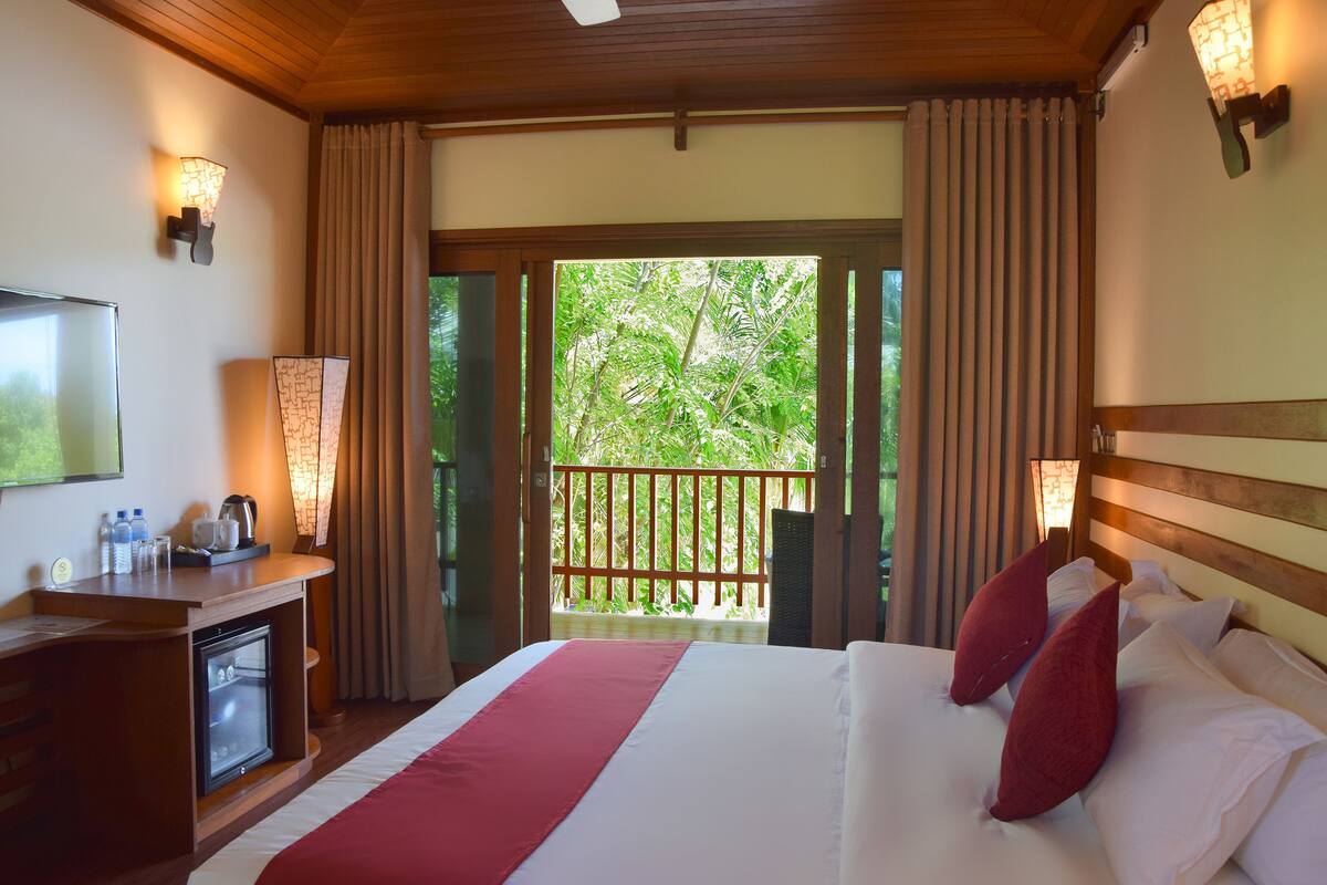 A hotel room with a bed, a desk with a refrigerator, a television, and a balcony with curtains.