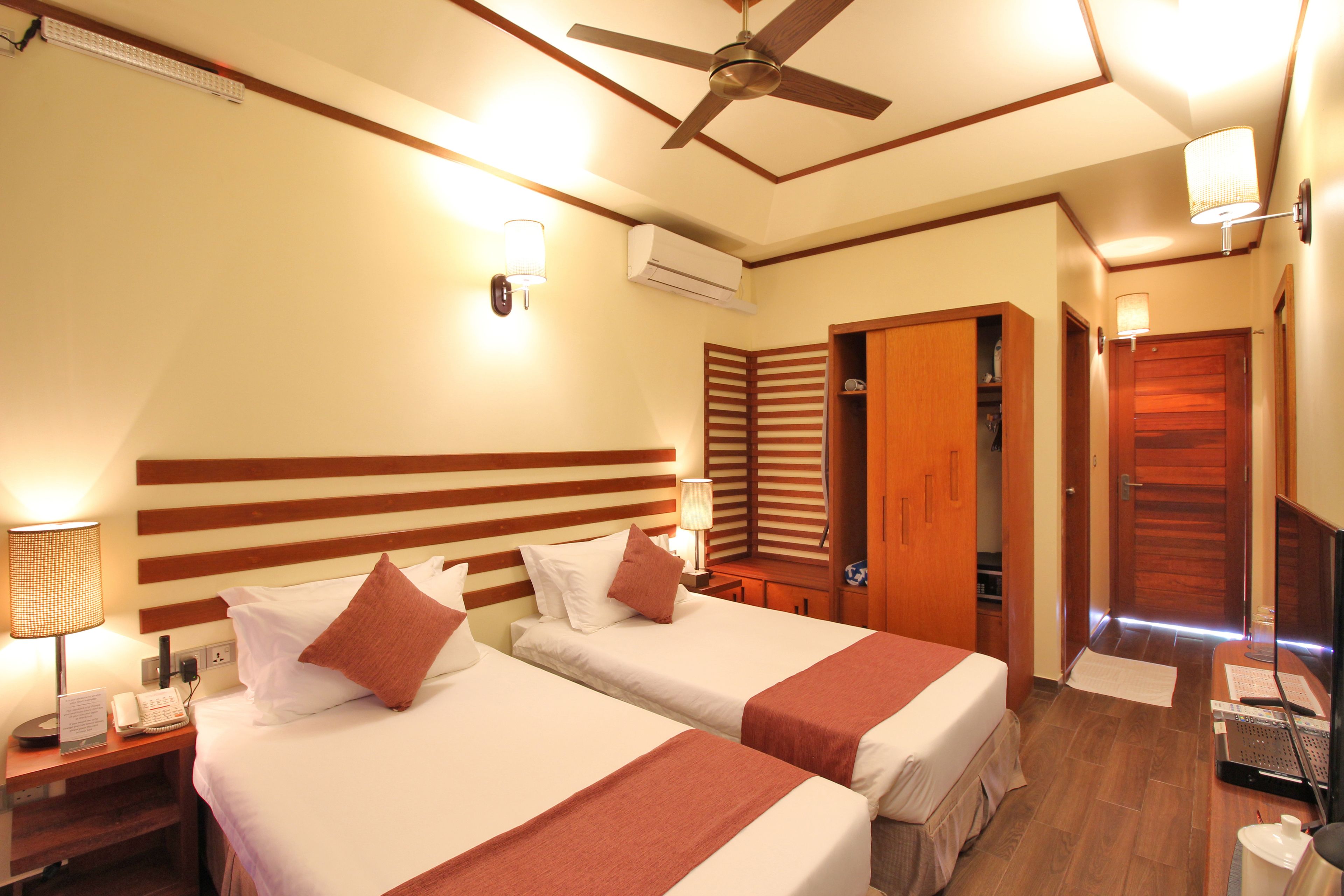 A hotel room with two beds, a ceiling fan, a desk with a computer, and a TV.