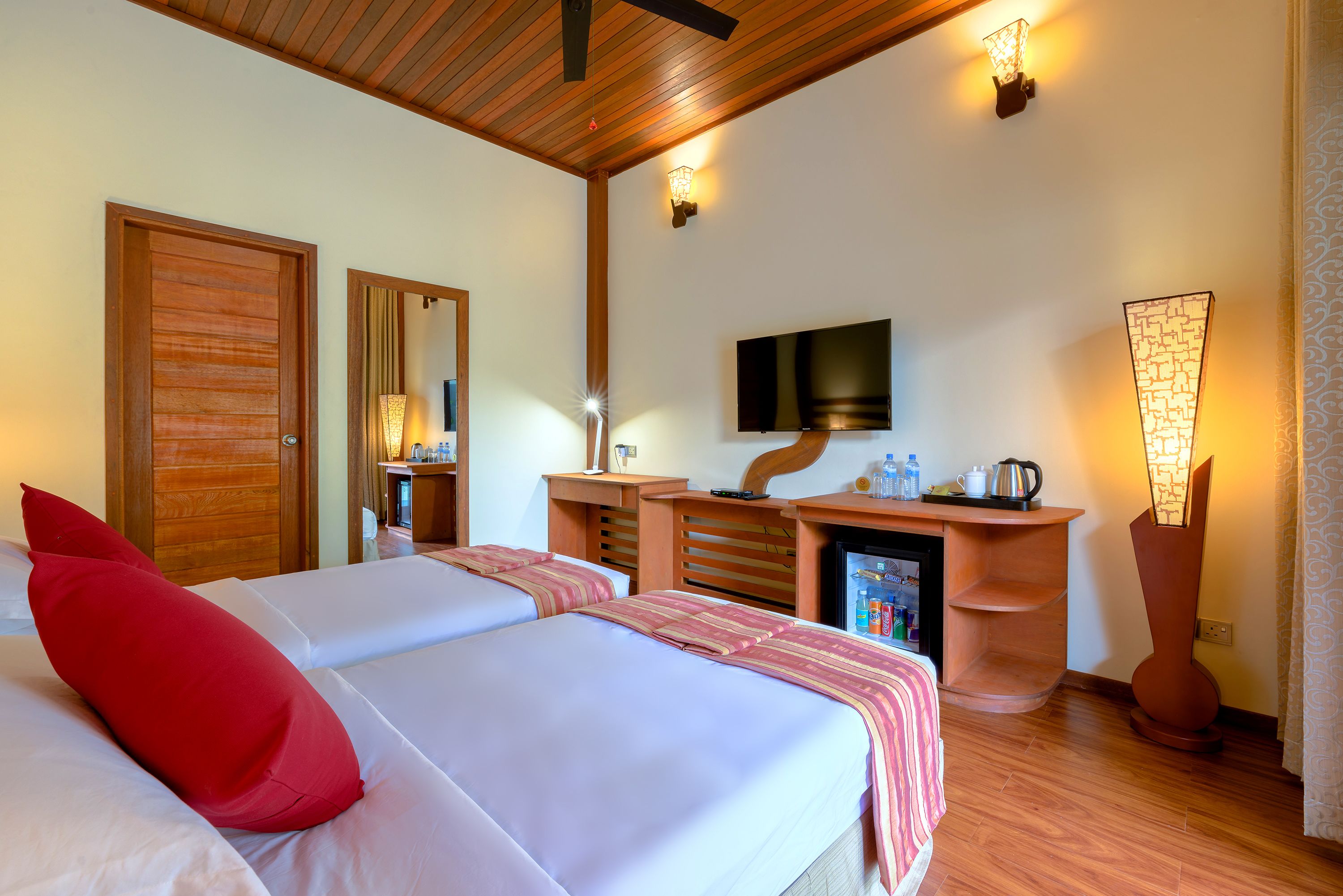 A hotel room with two beds, a TV, a minibar, and a desk with a lamp.