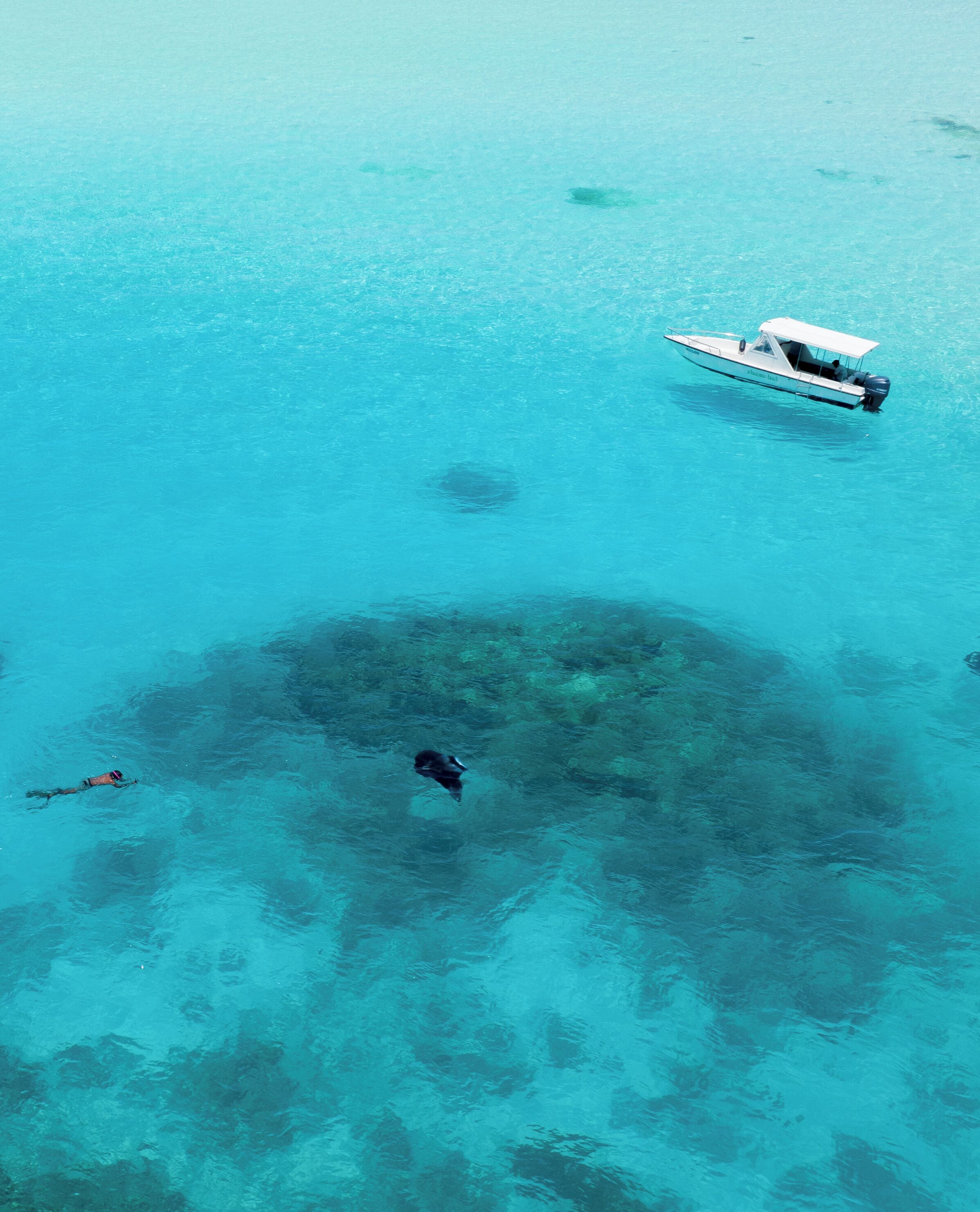 Vue aérienne d’une mer turquoise et limpide, avec un bateau et un plongeur.