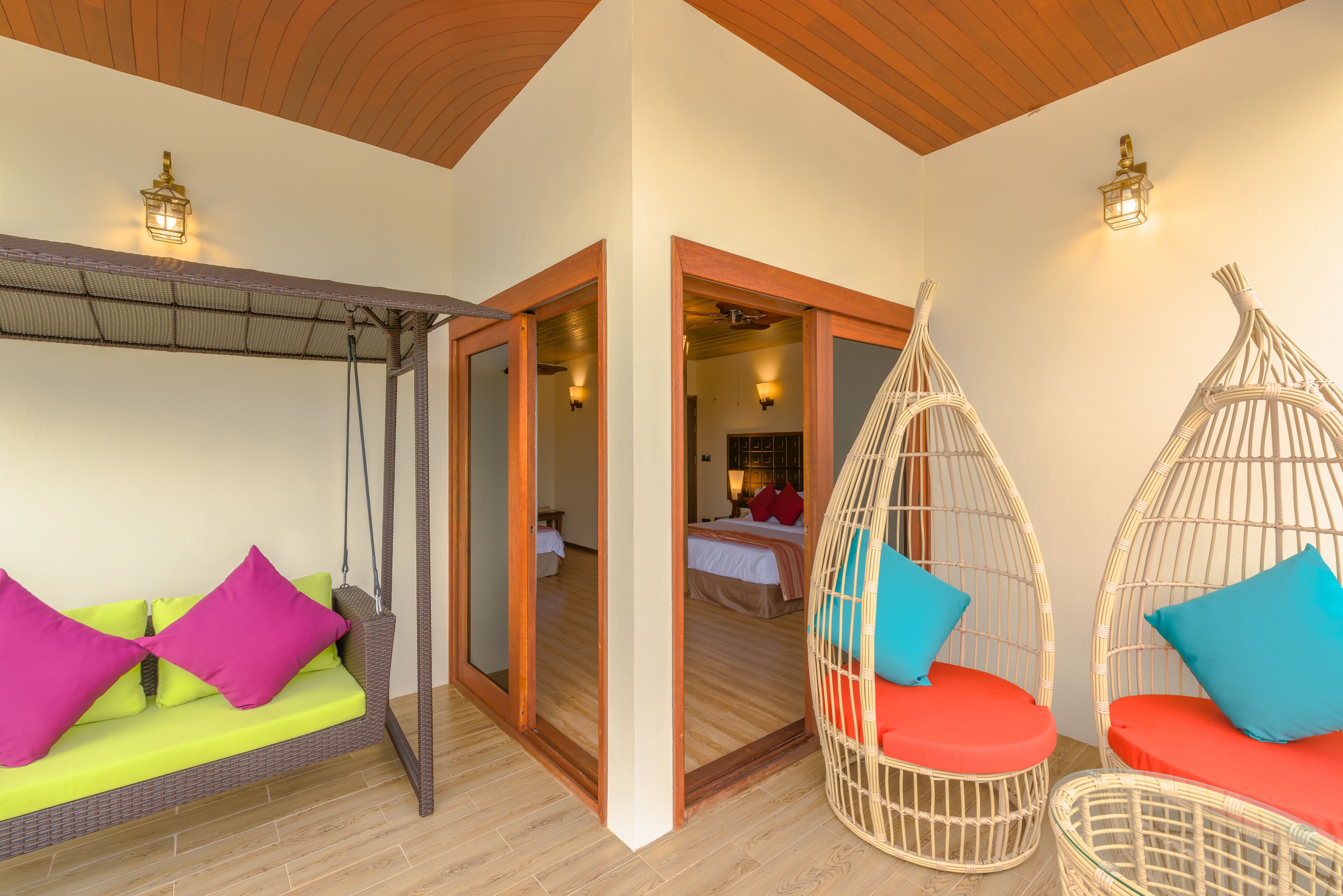 A room with a hanging chair, a sofa with bright cushions, and a bed in the background.