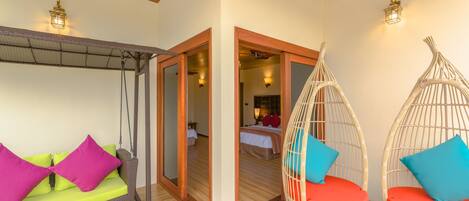 A room with a hanging chair, a sofa with bright cushions, and a bed in the background.