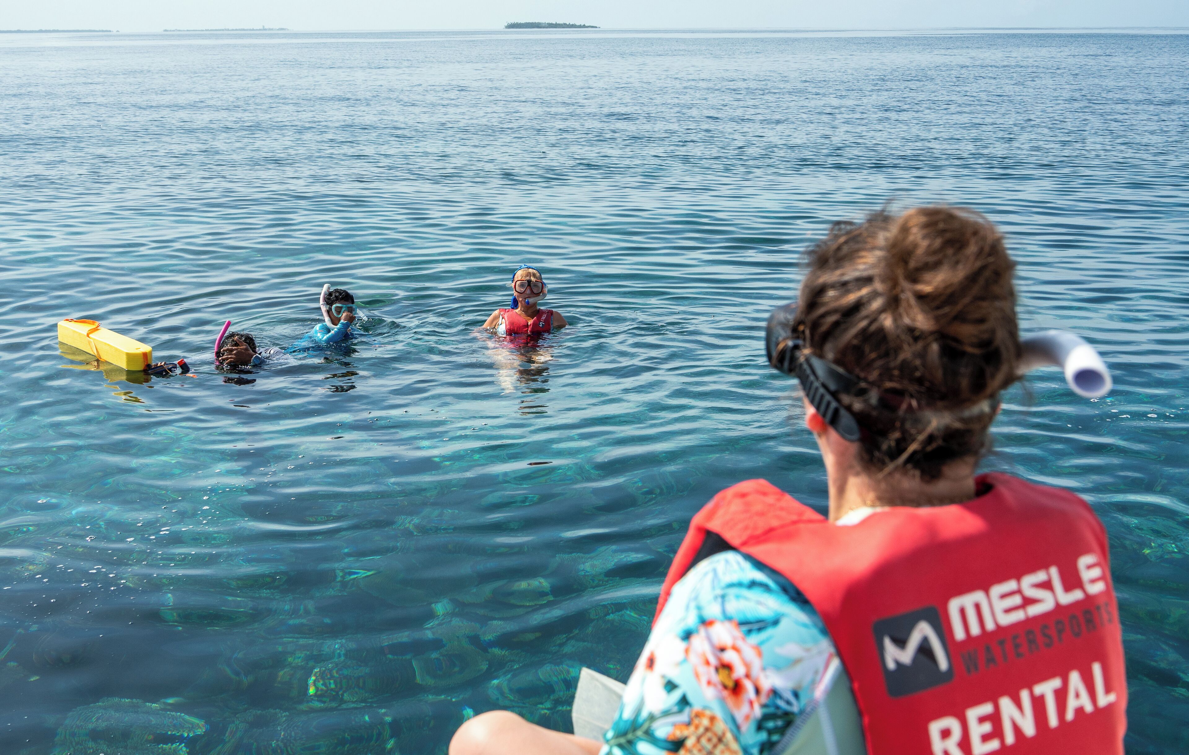 A person in a red life jacket with 'Mesle Watersports Rental' text, sitting on a boat.
