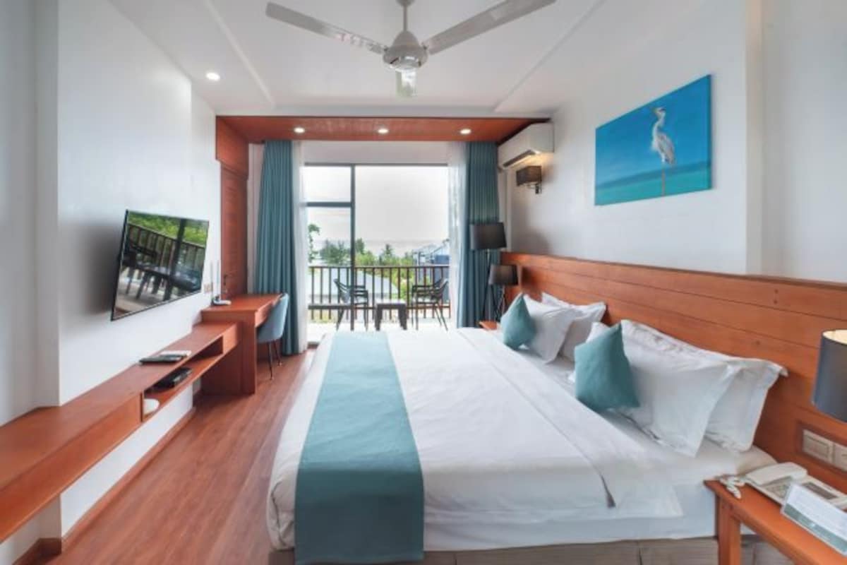 Habitación de hotel con cama, escritorio, televisión y balcón con sillas.