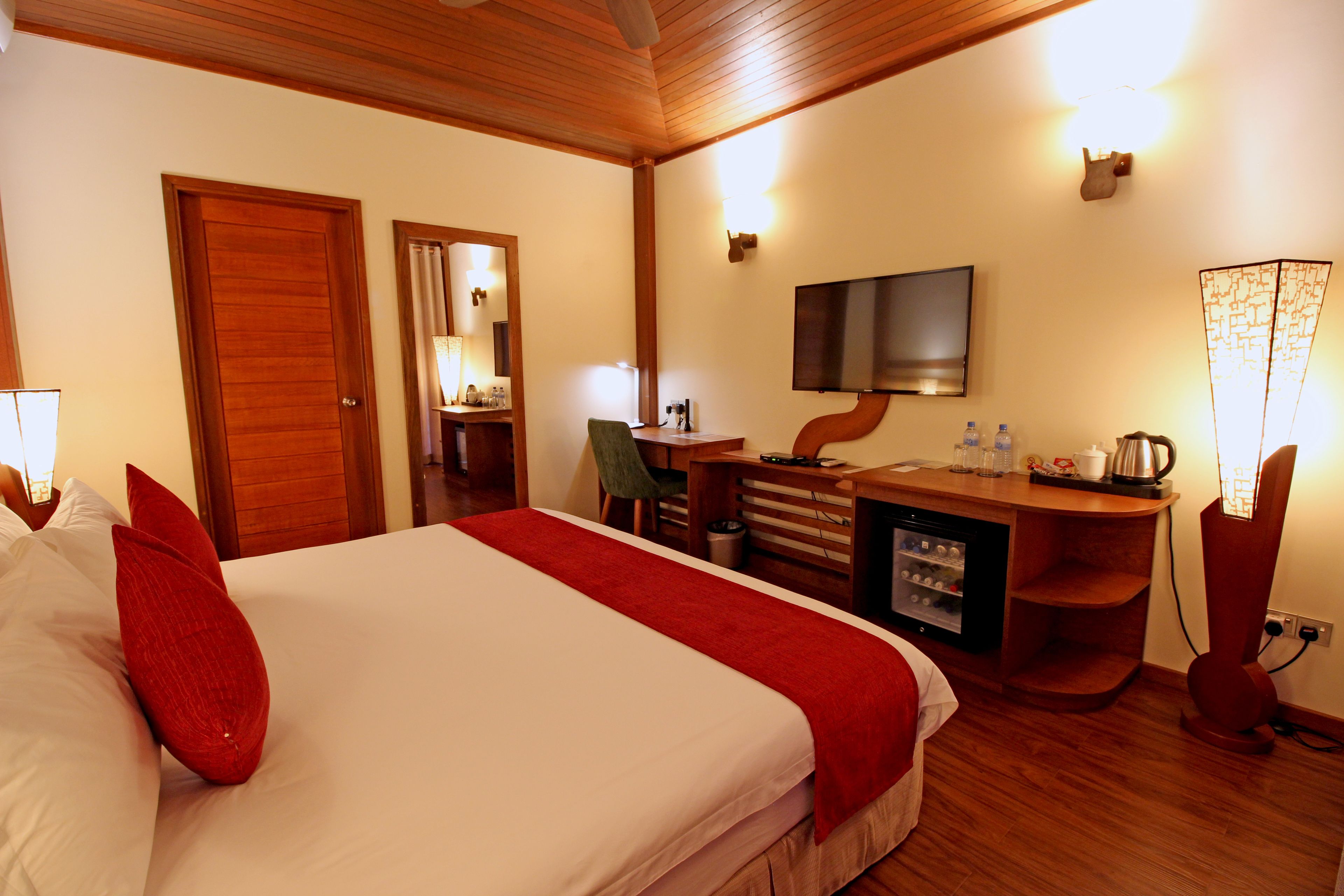 A hotel room with a bed, a desk, a chair, a television, and a minibar.