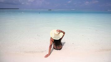Una persona sentada en la playa, con agua cristalina y un horizonte lejano.