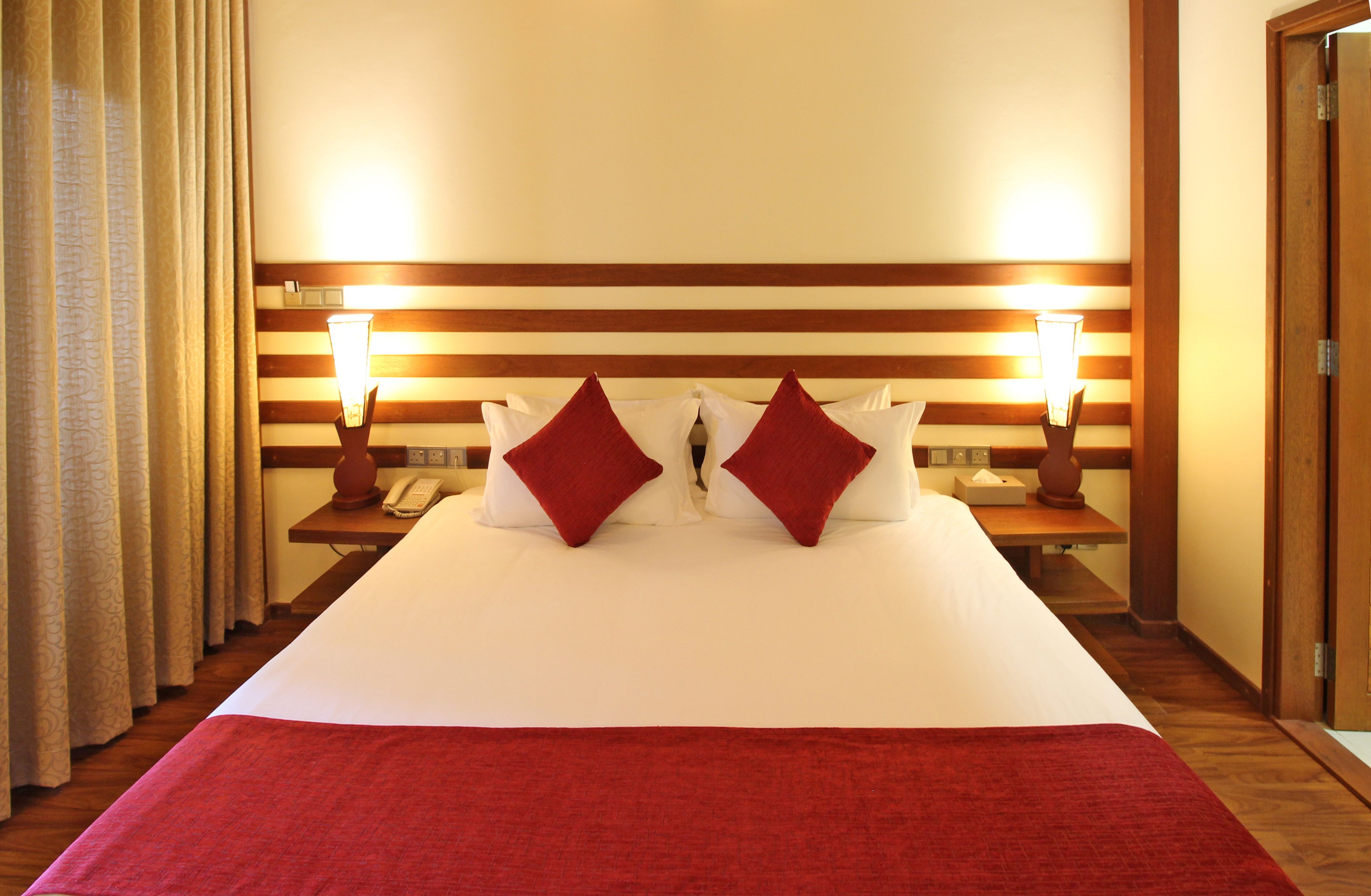 Une chambre d’hôtel avec un grand lit, deux lampes de chevet, un téléphone et une tête de lit en bois.
