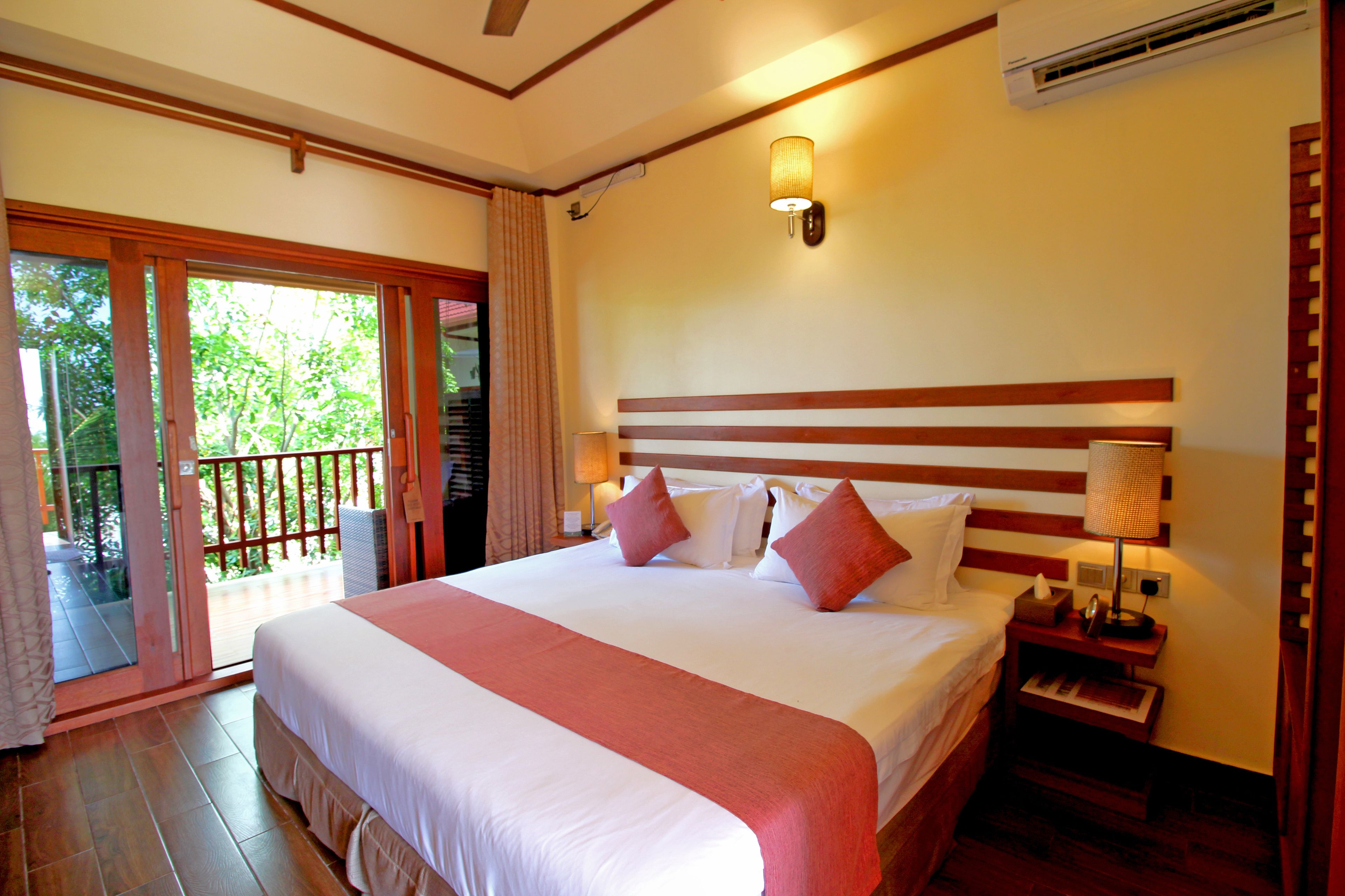 A hotel room with a large bed, a nightstand with a lamp, and a sliding glass door leading to an outdoor area.