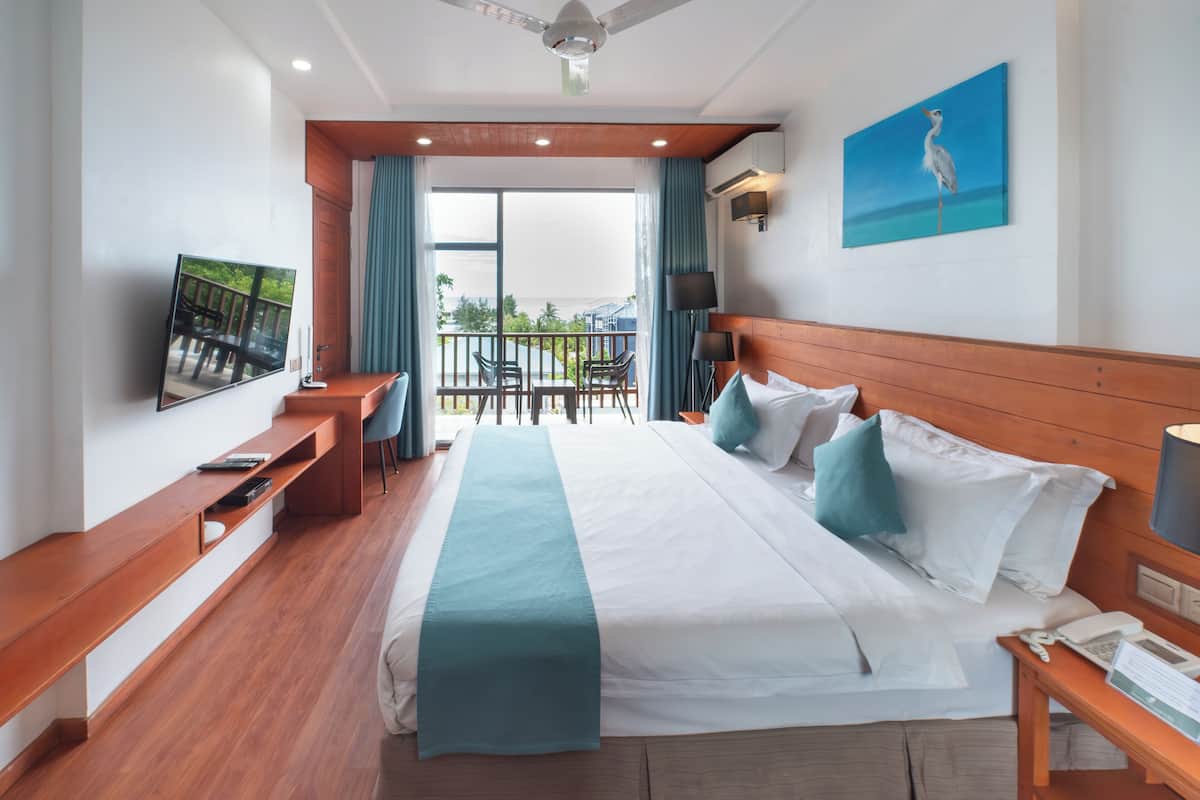 A hotel room with a large bed, a desk with a chair, a TV, and a balcony with a view.
